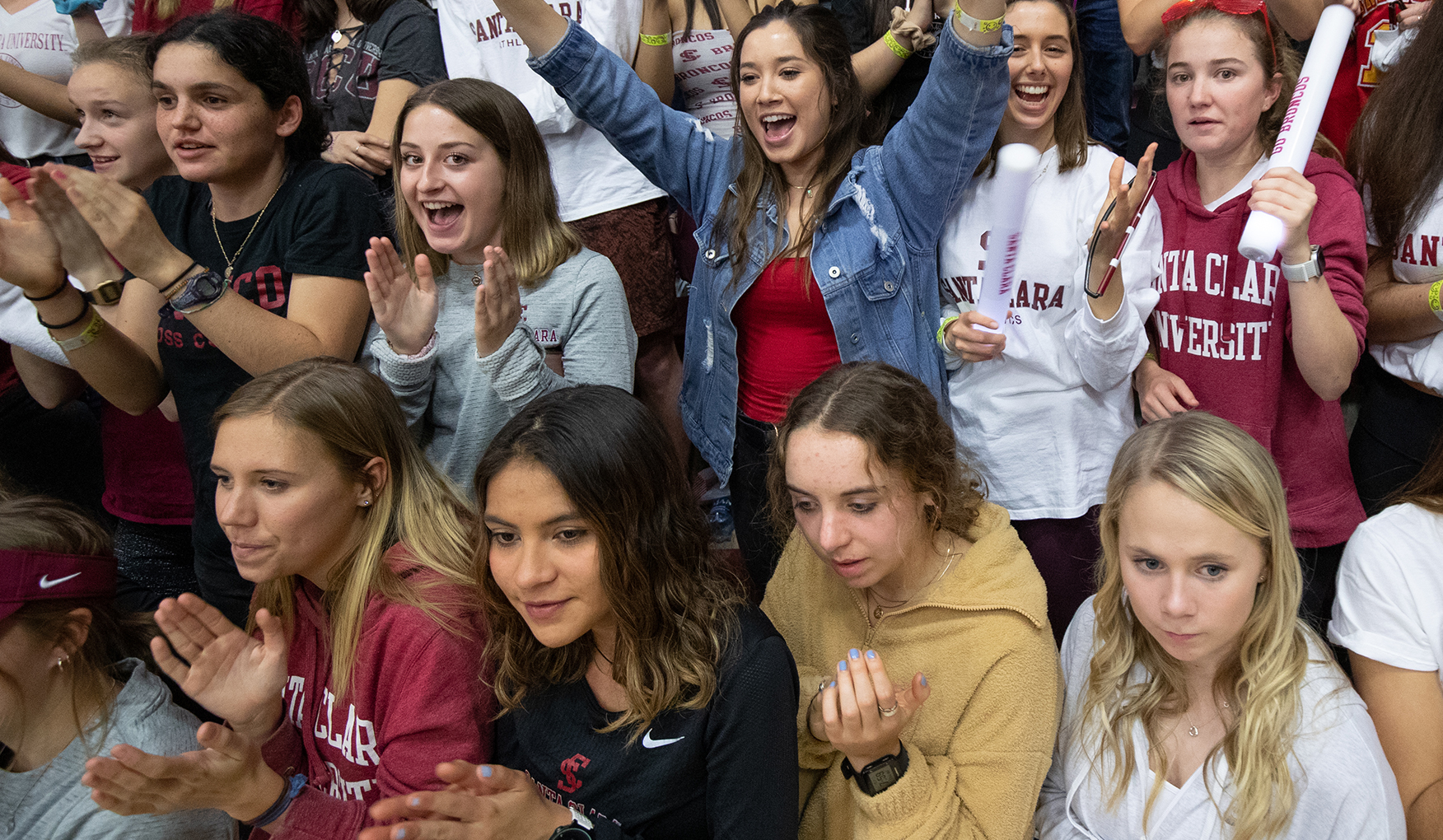 Santa Clara University students applauding and cheering at a basketball game, wearing school colors.