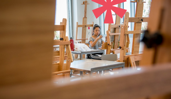 A Santa Clara student works on an art project in a well-lit studio with easels, art supplies, a laptop, and a smartphone on the table.