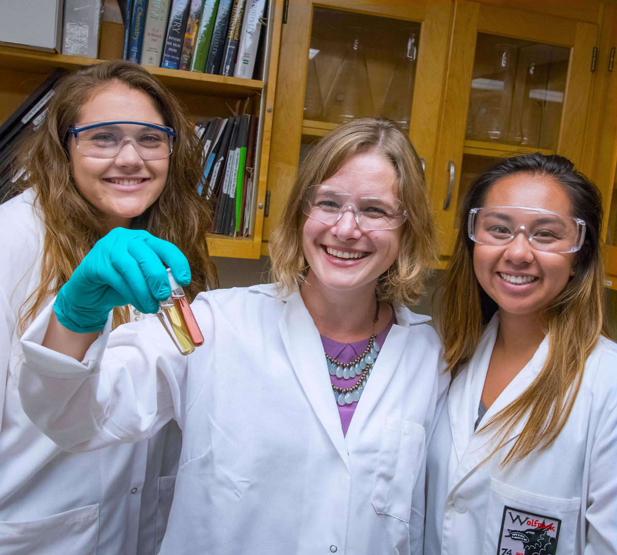 Two smiling female lab students, one holding three test tubes